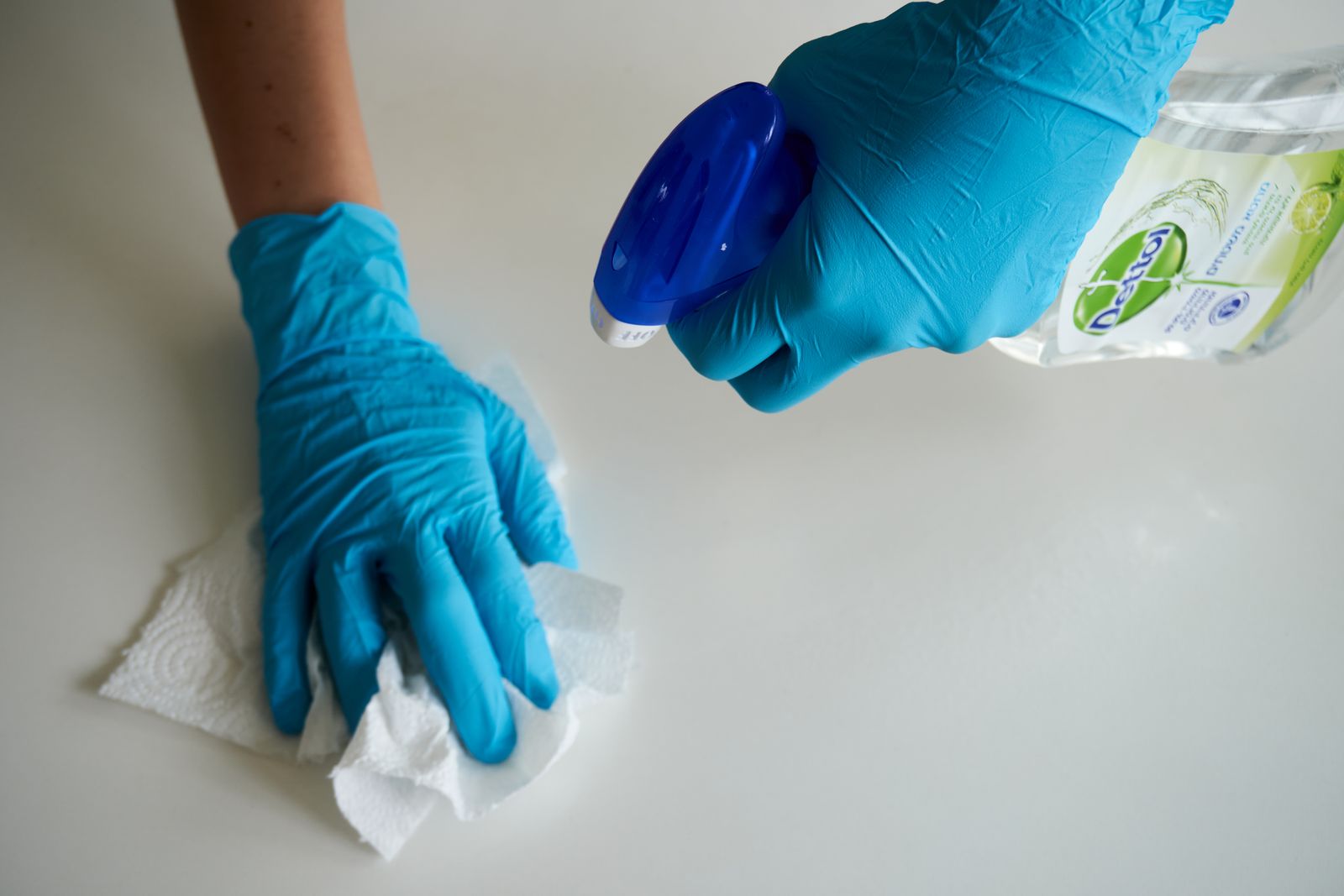 Persona con guantes desinfectando una superficie blanca