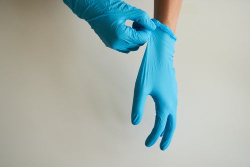 Free Close-up of hands putting on blue latex gloves against a neutral background. Stock Photo