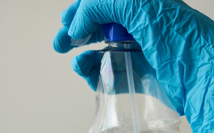 Close-up of a blue-gloved hand holding a cleaning spray bottle indoors.