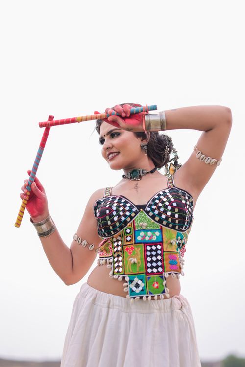 Free Woman in colorful traditional attire practicing Indian folk dance with dandiya sticks outdoors. Stock Photo
