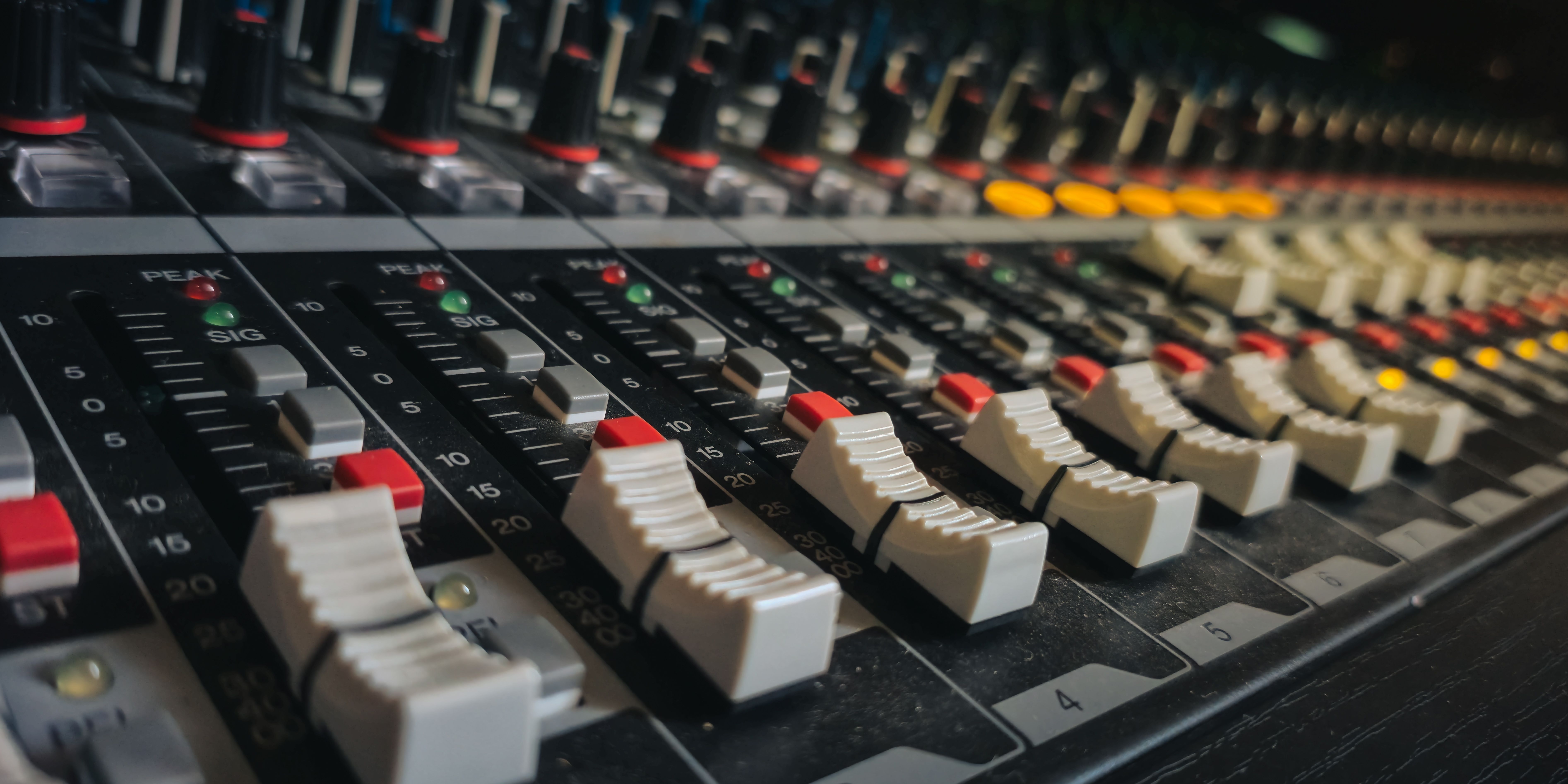 Close-up of an audio mixing console with sliders and knobs in a recording studio.
