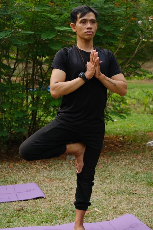 Free A man practicing yoga in tree pose outdoors in a Jakarta park, showcasing balance and mindfulness. Stock Photo
