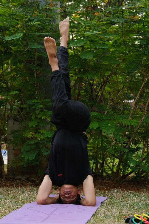 Free Man practicing headstand yoga pose on mat in Jakarta park, showcasing balance and strength. Stock Photo