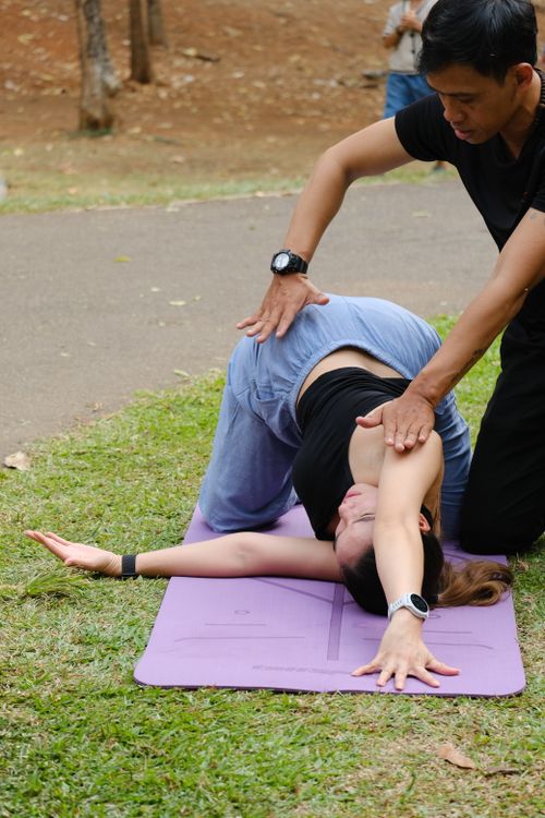 Free A person receiving yoga assistance in an outdoor park setting in Jakarta, Indonesia. Stock Photo