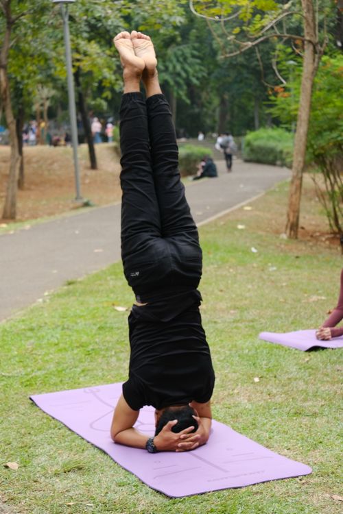 Free Adult man performing a headstand yoga pose on a mat in a park in Jakarta, Indonesia. Stock Photo