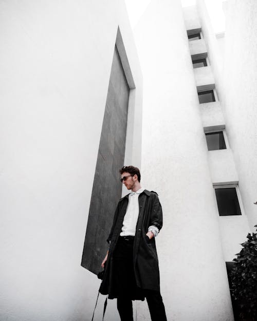 Man In Black Coat Standing Beside White Wall