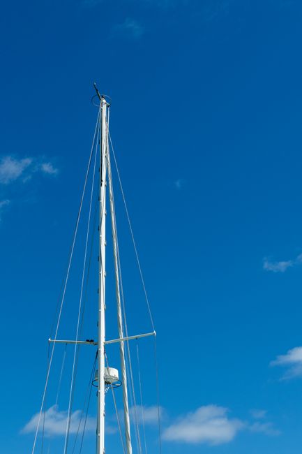 Vertical shot of a sailboat mast reaching into a clear blue sky, ideal for maritime themes.