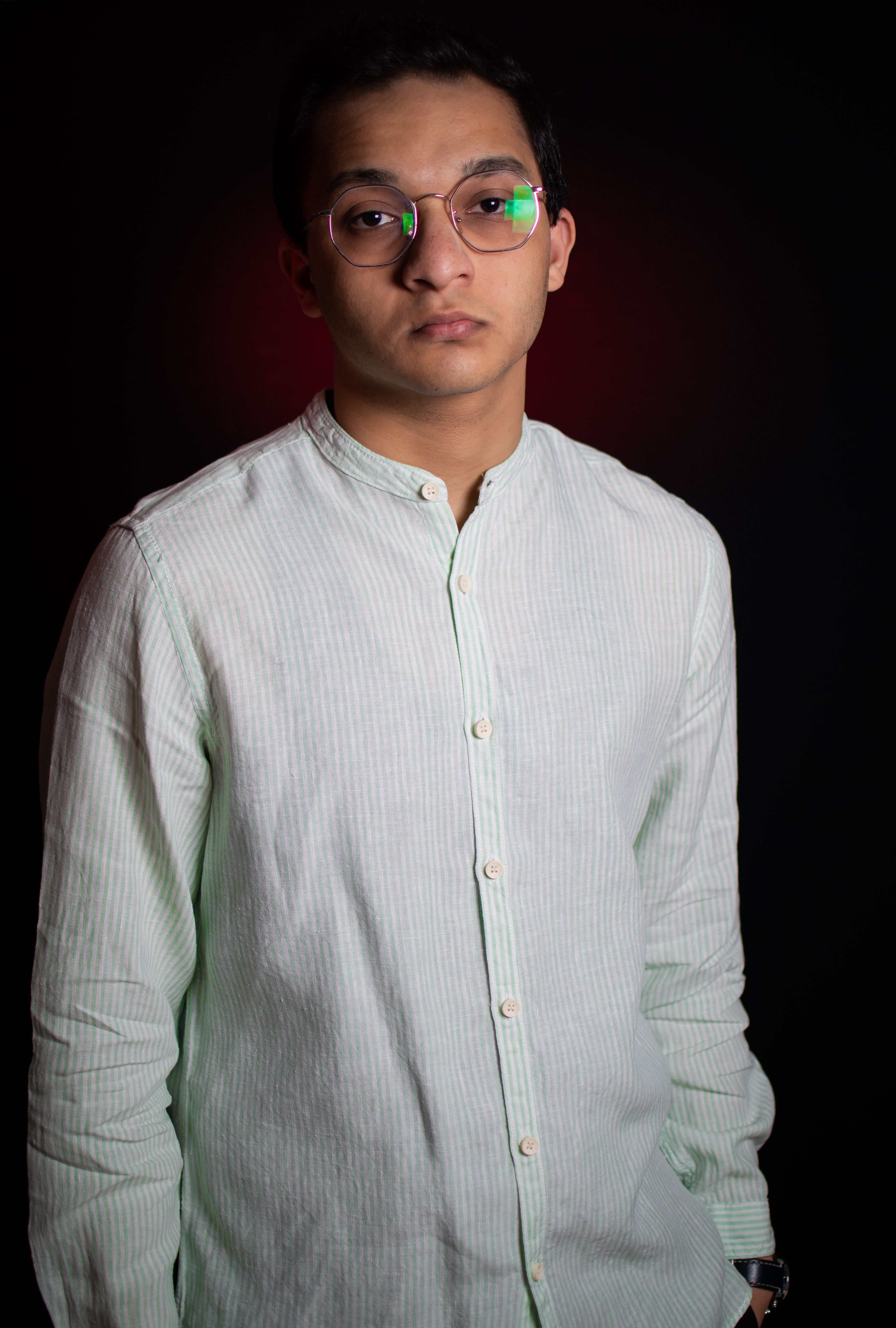A serious-looking man wearing glasses, posing against a black background.