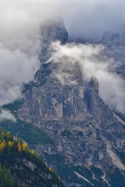 Free Majestic Dolomite peaks shrouded in mist and clouds, with autumnal forest below. Stock Photo