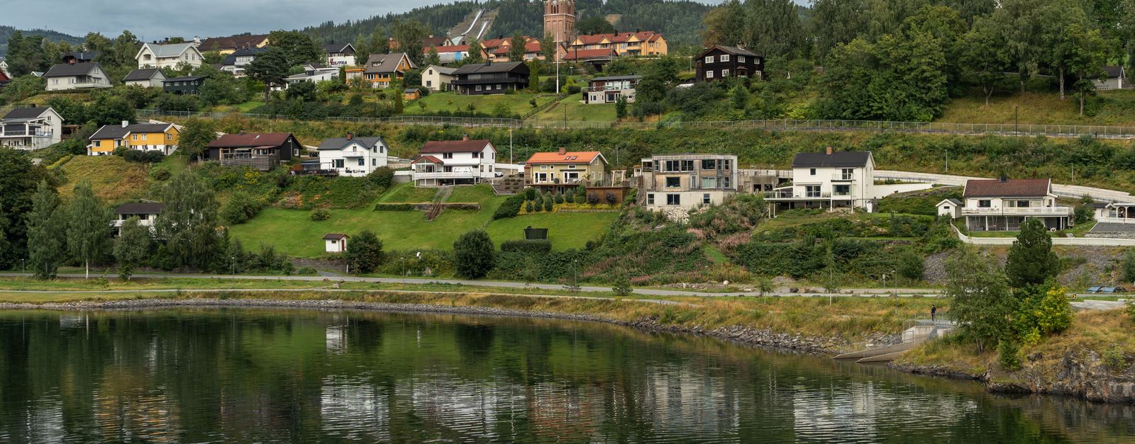 A picturesque Norwegian village with a church, reflecting on a calm river under a cloudy sky.