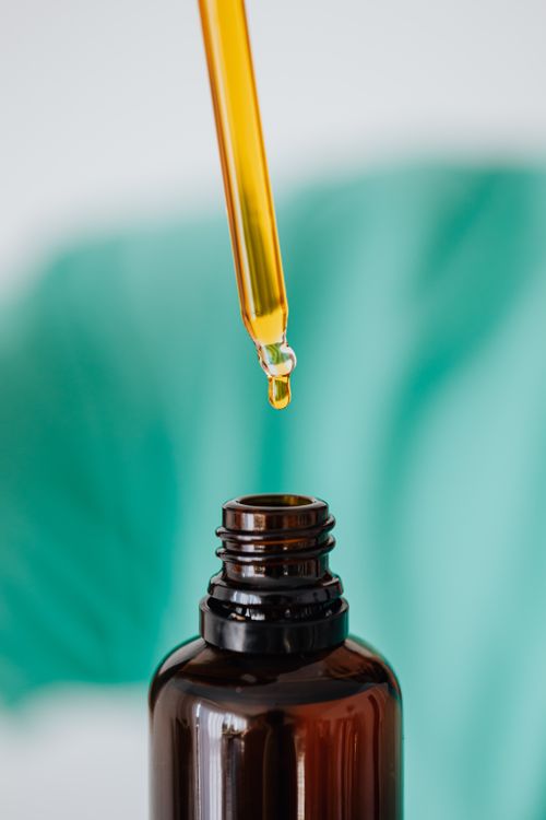 Free A dropper releasing oil into an amber bottle with a green background, showing skincare or essential oils concept. Stock Photo