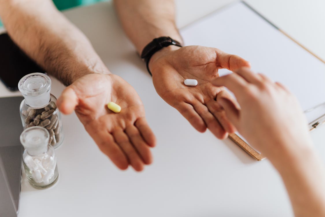 Free From above anonymous female and unrecognizable doctor man giving yellow and white tablets for choosing while working in modern clinic Stock Photo