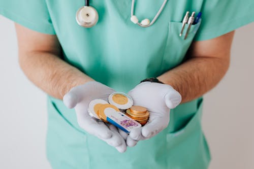 Unrecognizable medical worker demonstrating money wearing medicine form standing near white wall in hospital while working in day of salary