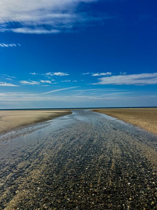 Free A tranquil view of a tidal stream flowing toward the ocean under a vivid blue sky with wispy clouds. Stock Photo
