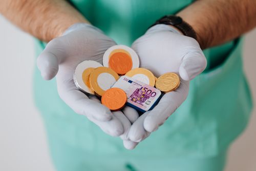 Free From above crop anonymous medical worker in rubber disposable gloves holding in hands chocolate coins Stock Photo