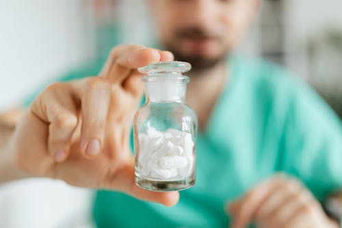Free Crop medical worker holding in hand glass transparent bottle while showing white tablets Stock Photo