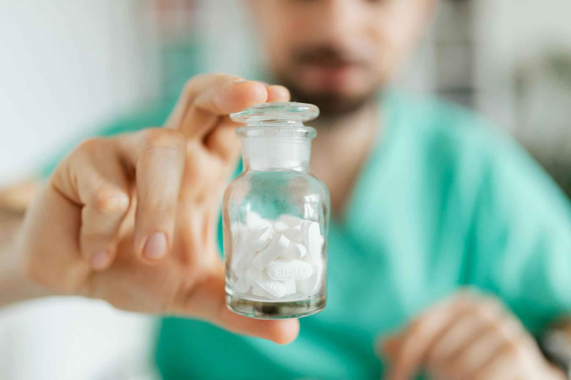 Crop medical worker holding in hand glass transparent bottle while showing white tablets