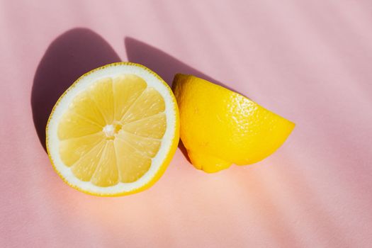 阳光下，粉红背景上新鲜多汁的柠檬半顶视图