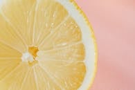 Closeup of slice of fresh juicy bright lemon placed on smooth pink surface