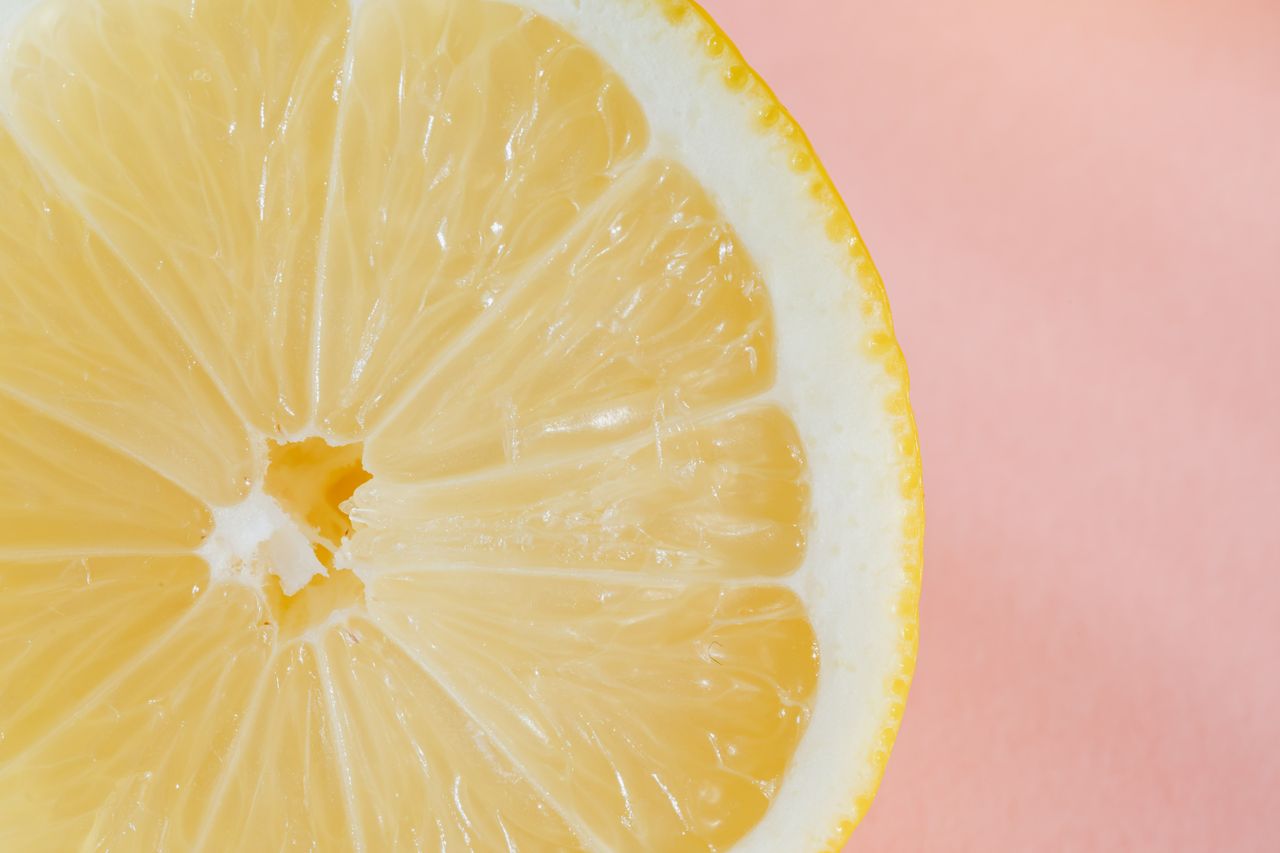 closeup of slice of fresh juicy bright lemon placed on smooth pink sur