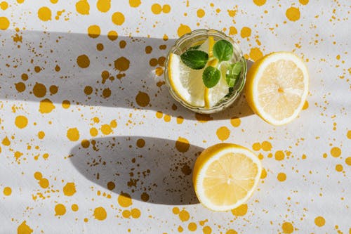 Top view of glass of fresh cold drink with halves of lemon on table with white tablecloth in yellow blots