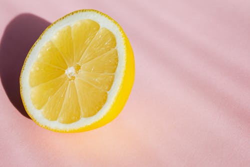 From above half of fresh sliced lemon placed in pink background in bright sunlight