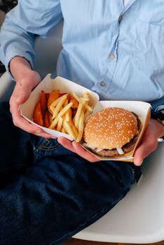 A person holds a cheeseburger and fries on their lap, ready to enjoy a fast food meal.
