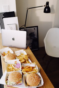 From above of various fast food and opened laptop placed on wooden table in creative place