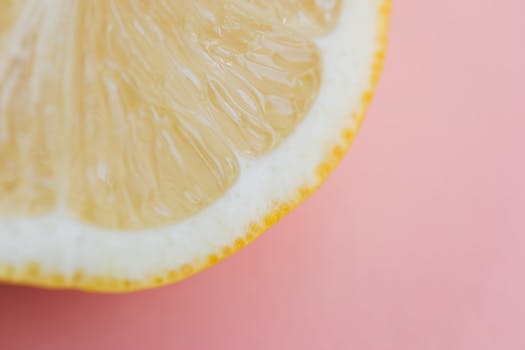 Detailed macro shot of a fresh lemon slice on a pastel pink background, perfect for food and health themes.