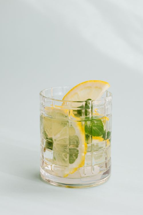 Free Flat lay of glass of cold fresh drink with slices of lemon and leaves of mint placed on white background Stock Photo