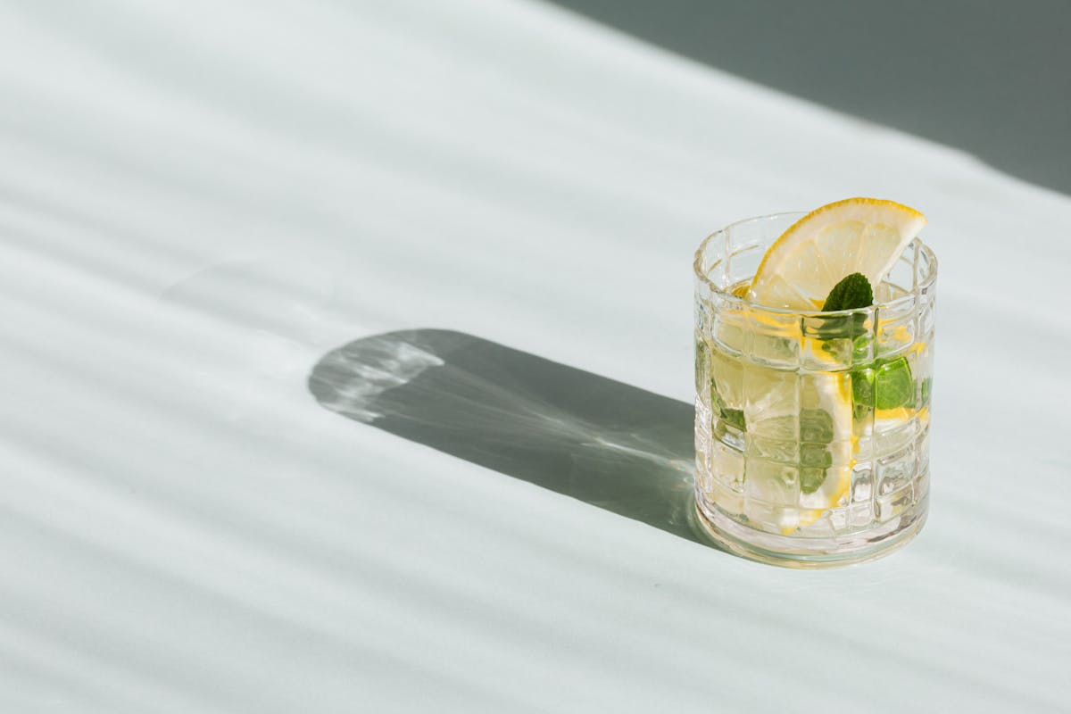 Flat lay of glass of fresh beverage with slices of lemon and leaves of mint placed on white background