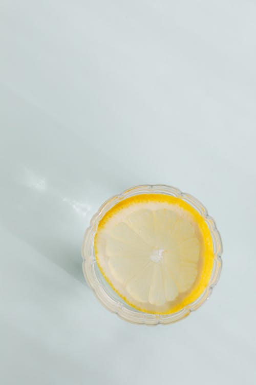 Top view of glass of refreshing beverage with slice of lemon placed on white background