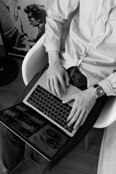 From above of anonymous male in casual clothes sitting on chair and using laptop while working on business project remotely