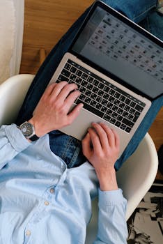 Overhead shot of person in jeans typing on a laptop, creating a comfortable workspace ambiance.