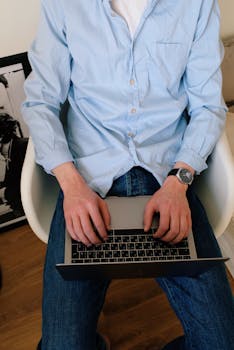 Man in casual attire using laptop indoors, ideal for remote work concepts.