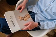 From above of unrecognizable man in casual clothes resting with magazine Kinfolk on knees while sitting on chair in modern studio