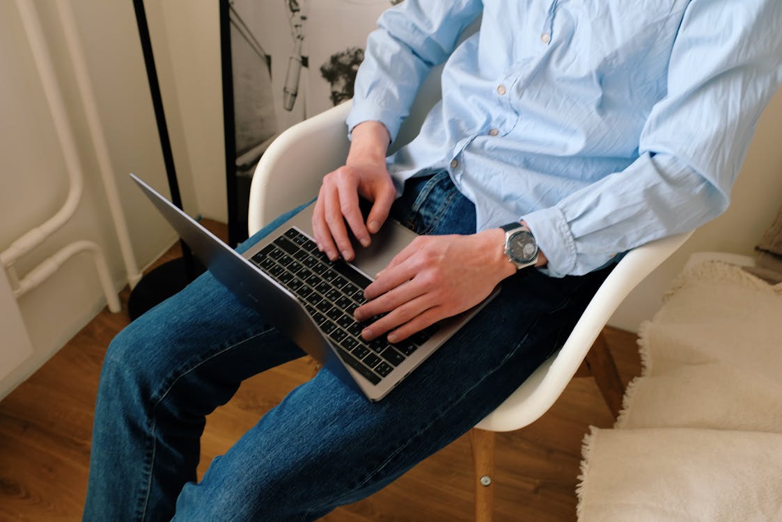 Free Crop unrecognizable guy browsing laptop in living room Stock Photo