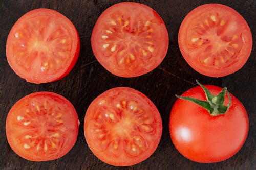 Top view closeup of fresh halves of ripe tomatoes with juice on cut side and whole tomato placed on wooden cutting board