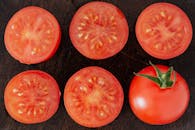 顶视图特写：木砧板上放着半块新鲜的成熟番茄，切边有汁