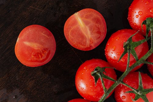 From above closeup of cut on halves fresh tomato and branch of ripe tomatoes with drops placed on wet wooden cutting board