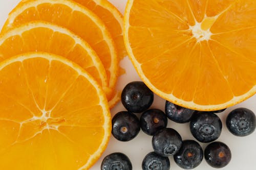 Top view closeup of round form slices of orange and bunch of ripe blueberries on white background