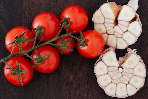 From above of branch of ripe tomatoes and cut garlic on halves placed on wooden table