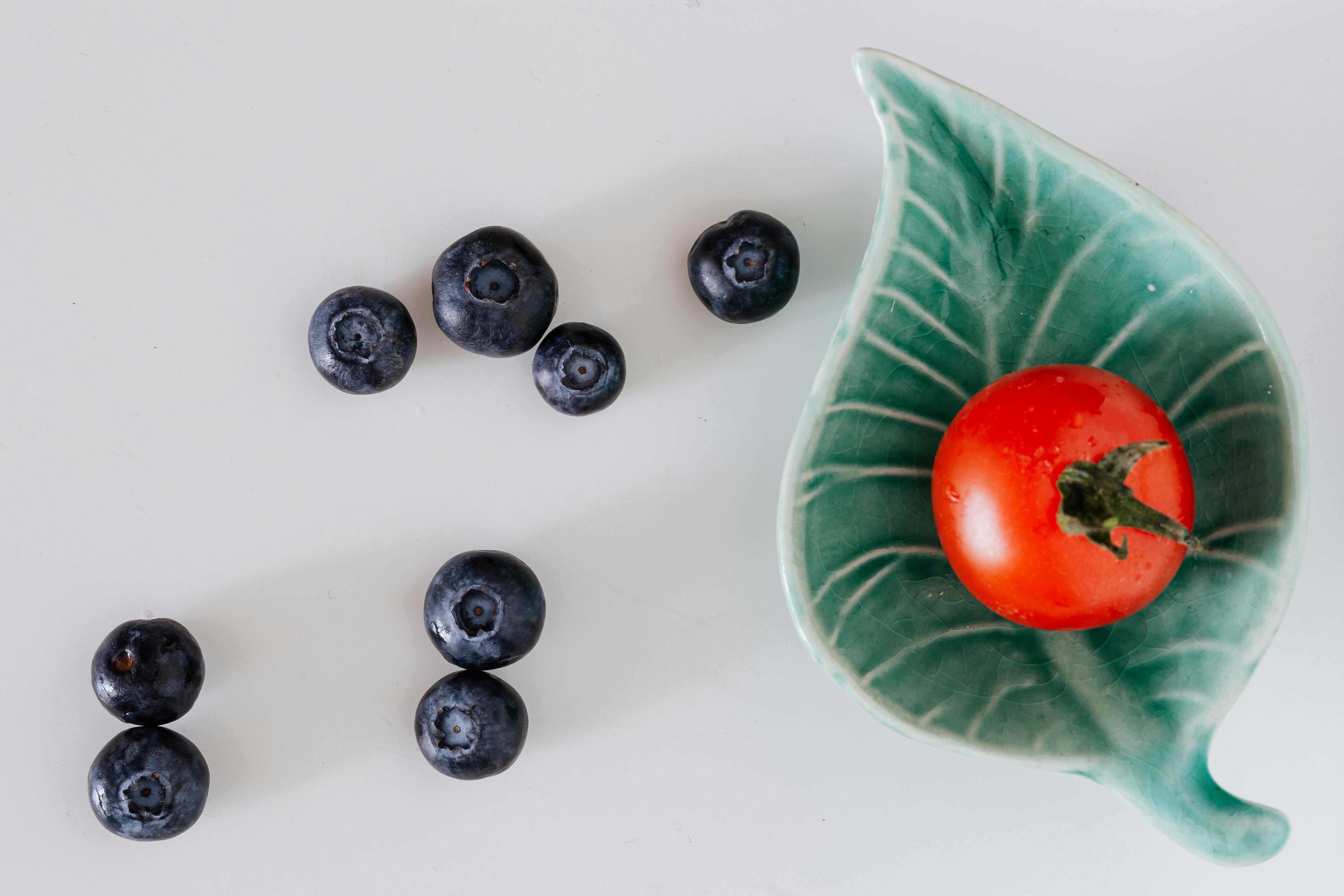 minimalistic composition of fresh tomato on small designer platter near blueberries on gray background