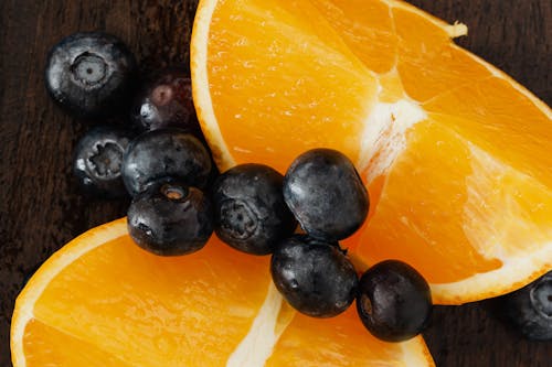 From above organic blueberries scattered on halves of ripe orange on lumber table prepared for raw breakfast