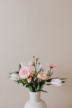 Composition of white ceramic vase with delicate carnations and white tulips with elegant pink Gerberas and green leaves