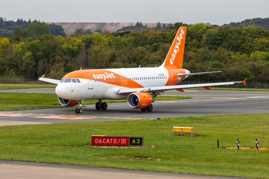 EasyJet Airbus A320 taxiing at a Scottish airport runway, surrounded by lush greenery.