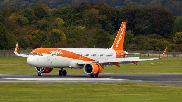 EasyJet Airbus A320 Neo taxiing on a runway in Scottish landscape.