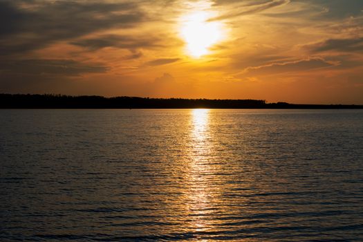 Serene sunset scene over a tranquil lake in Felixlândia, Brazil, with vibrant orange and yellow hues reflecting on the water.
