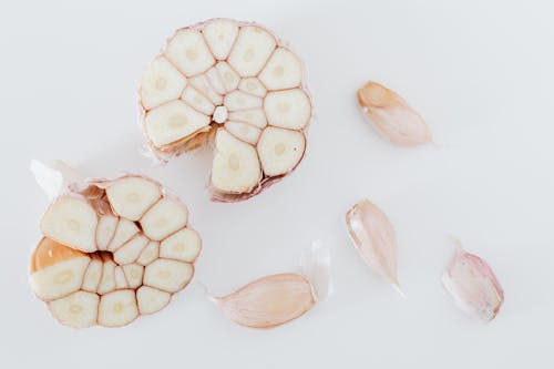 Top view of composition with garlic cut in half and pieces placed on white surface of table