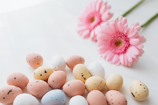 A vibrant still life of pastel Easter eggs and pink flowers on a white background.